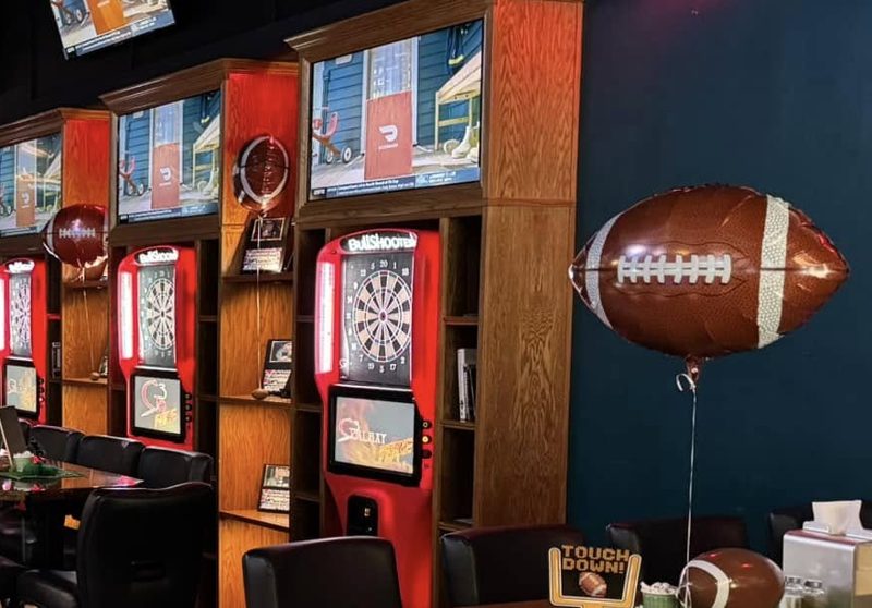 Red electronic dart machines under TVs, decorated for game day